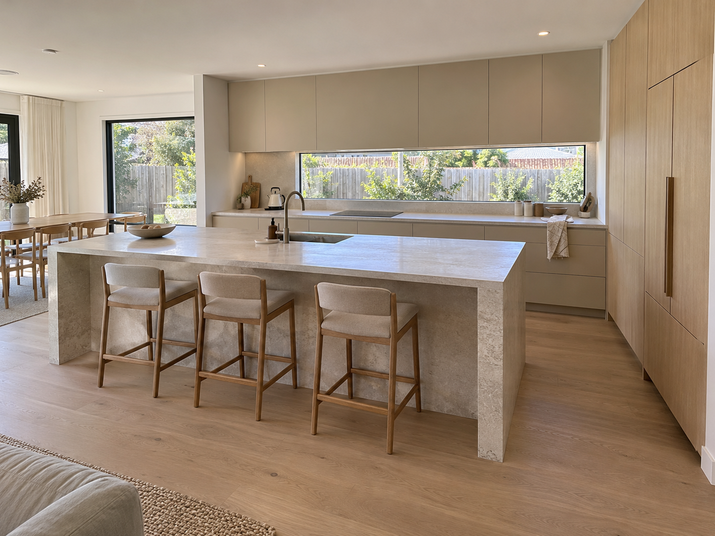 Spacious modern kitchen concept with sand-coloured cabinets, an oak pantry wall and a large stone island